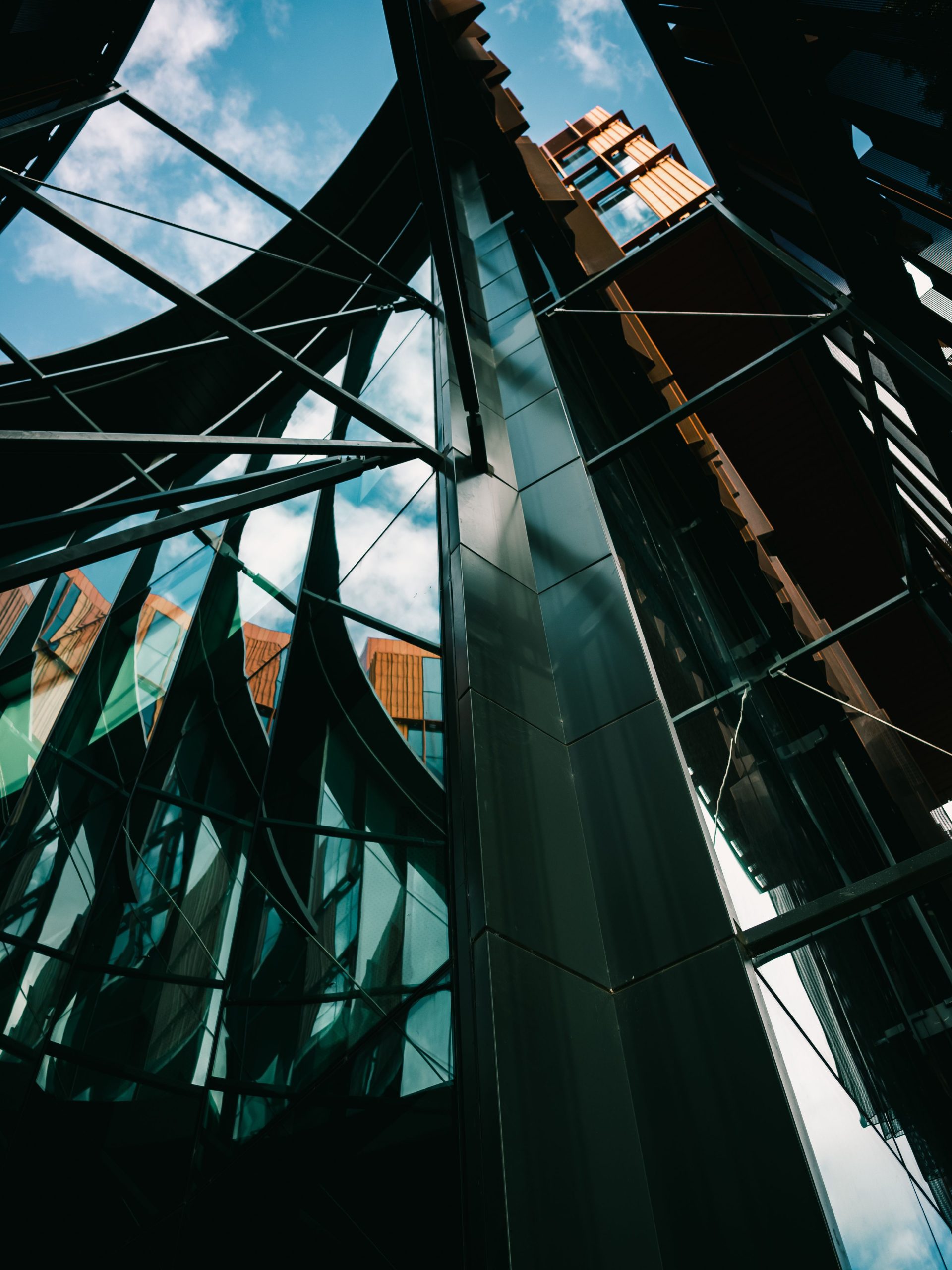 Dynamic low angle view of a modern glass building with unique reflections and a bright sky.