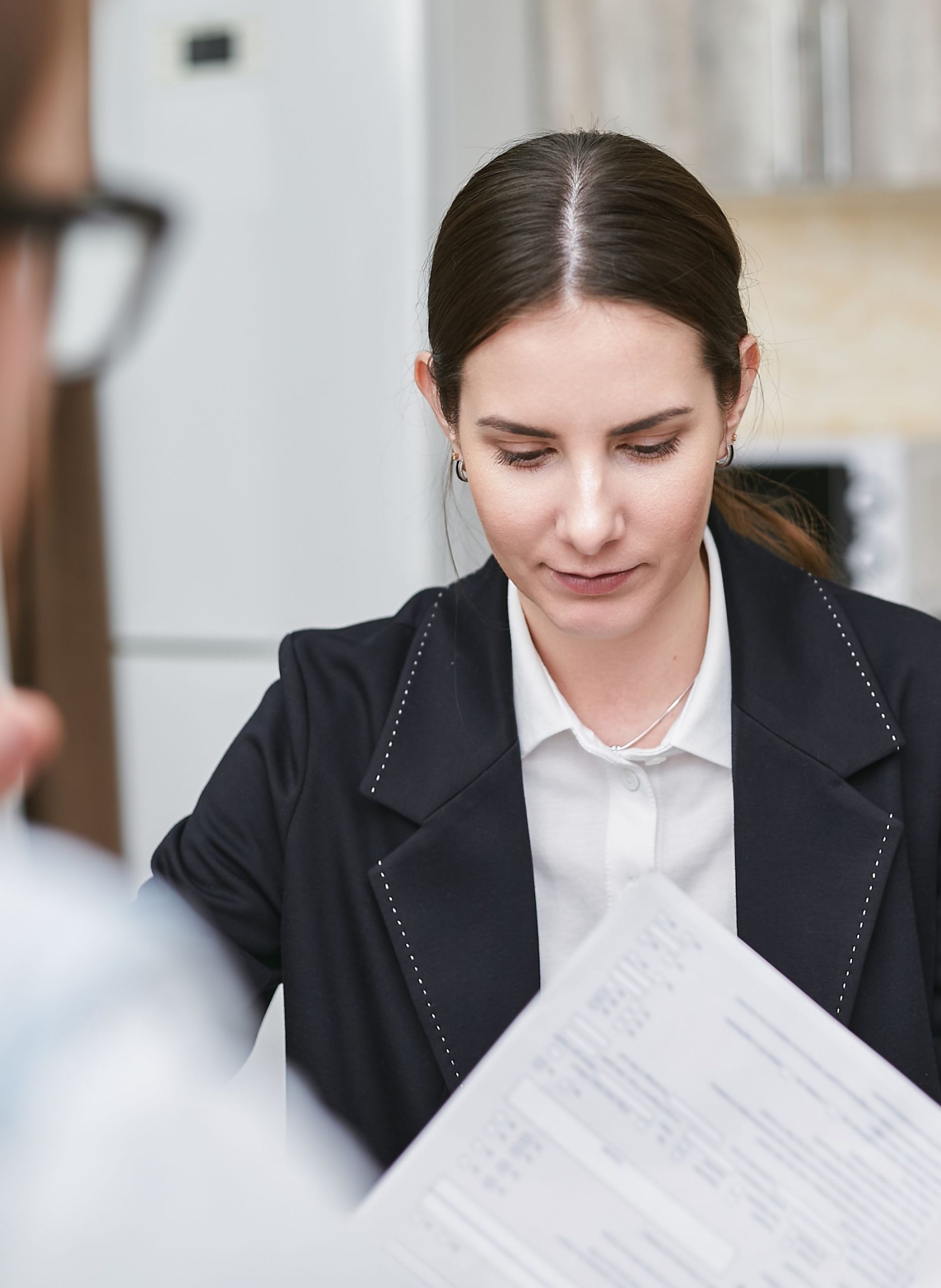 Focused woman in a black blazer reviewing an important document indoors.